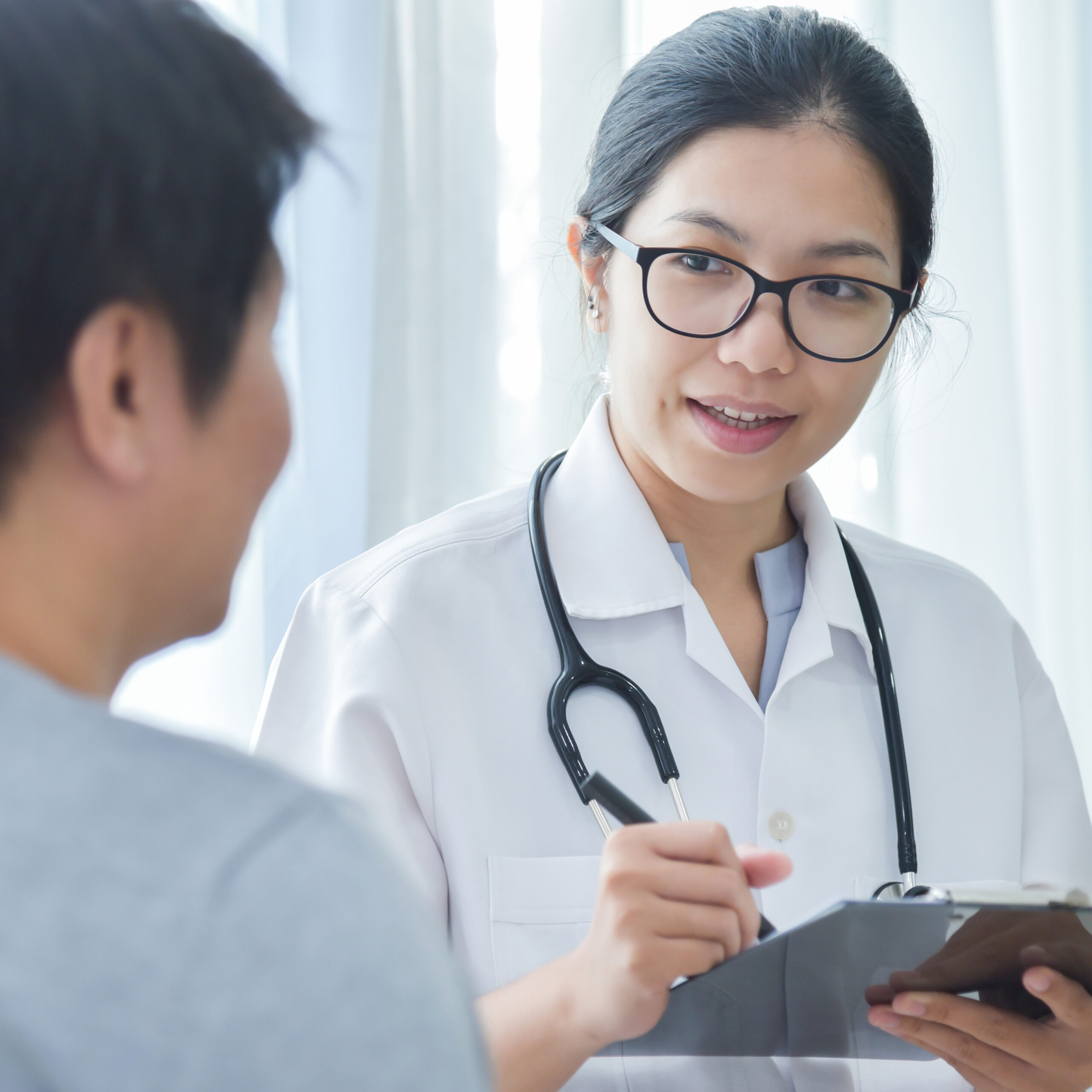 Asian female doctor taking notes while talking to patient.