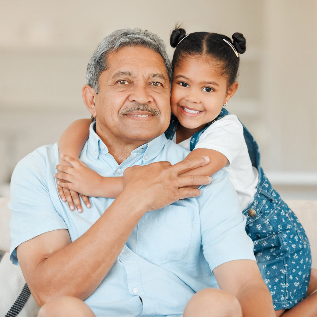 Latin grandfather with granddaughter smiling at camera.